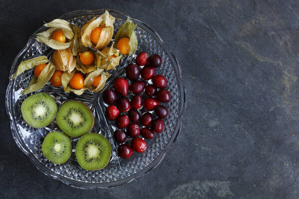 Physalis fruit - Cape gooseberries with cranberries and kiwi on cut glass platter on slate background - with copy space