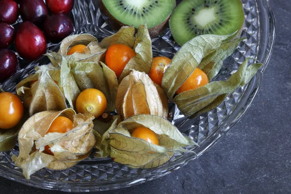 Close-up of Physalis fruit - Cape gooseberries with cranberries and kiwi on cut glass platter on slate background - with copy space
