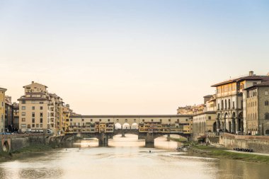 O gün batımında arka planda açık bir gökyüzü ile Floransa geçerken Ponte Vecchio Arno Nehri üzerinde göster
