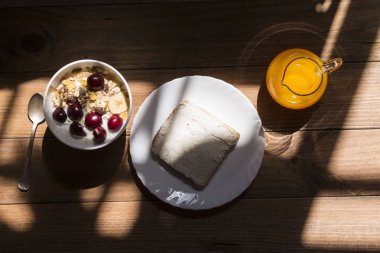 Kase müsli ve meyveler krem peynir ve bir masanın üzerine düzenlenmiş ve ışık ve gölge bir efekt oluşturarak bir pencere ışığıyla aydınlatılan portakal suyu, yoğurt.
