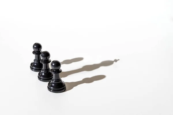 Three chess pawns casting shadow, two of them their own shadow and the third the shadow of the king. Conceptual photography that can illustrate concepts such as leadership, power, among others