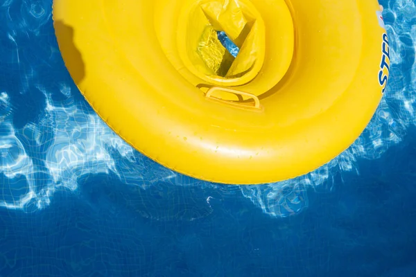 Yellow rubber ring floating in a pool with reflections in the water.