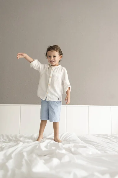 Çocuk bir yatak üstünde duran, atlama ve el hareketi.