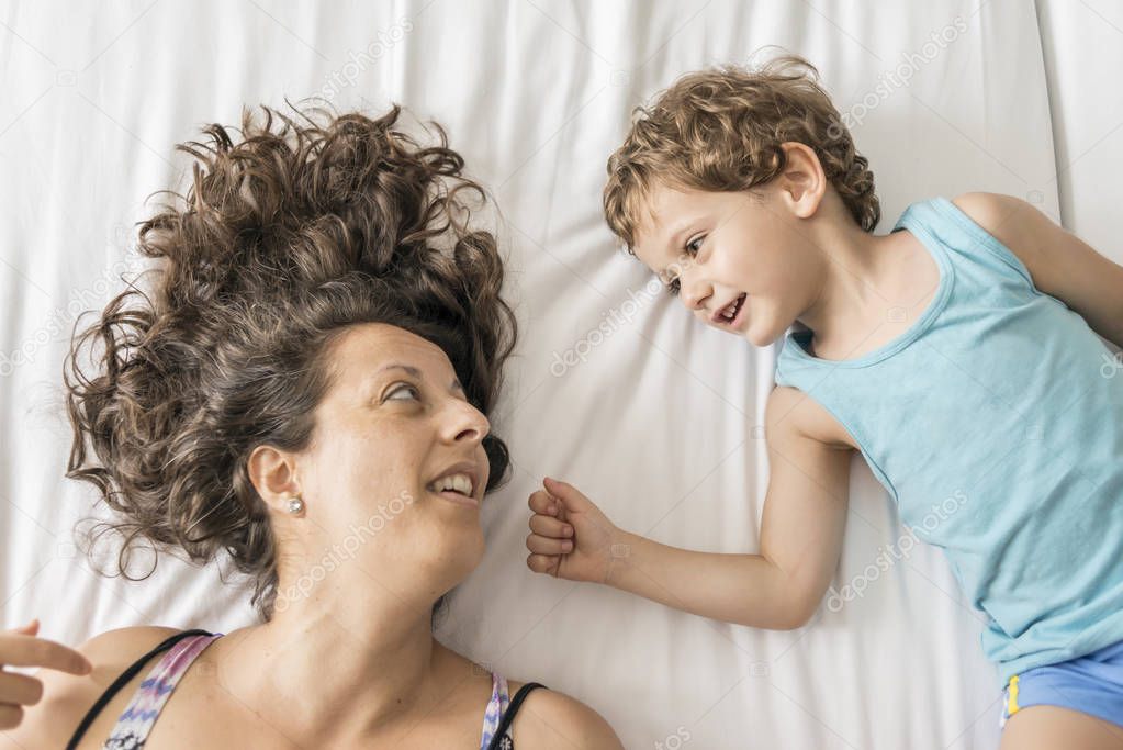 A woman and her son playing in bed and gesturing.