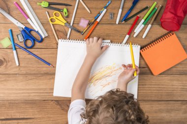 Okula geri kavramı. Ahşap kurullarında yalan ve okul malzemeleri bir defter üzerinde karalama çevrili çocuk.