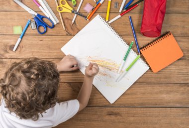 Okula geri kavramı. Ahşap kurullarında yalan ve okul malzemeleri bir defter üzerinde karalama çevrili çocuk.