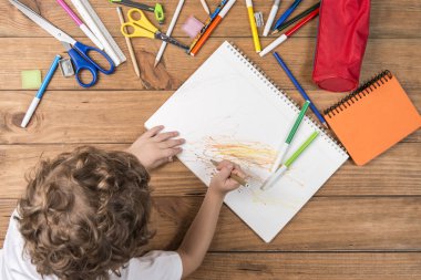 Okula geri kavramı. Ahşap kurullarında yalan ve okul malzemeleri bir defter üzerinde karalama çevrili çocuk.