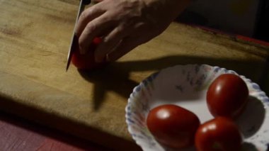 Ahşap bir tahta üzerinde bıçak ile bir domates kesme ellerin detay atış.