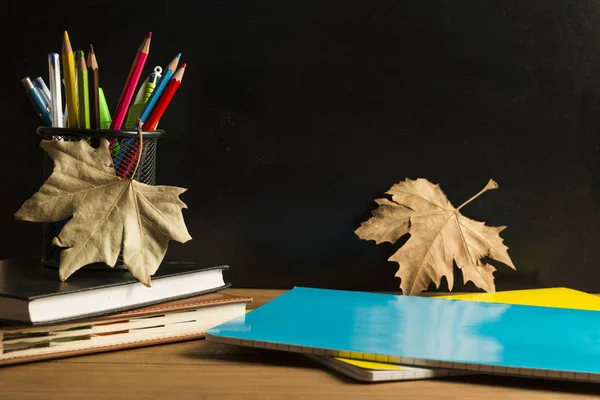 黒板を背景にした木製のボードに、本、ノート、学用品、紅葉. — ストック写真