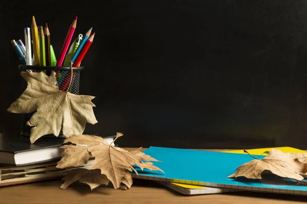 黒板を背景にした木製のボードに、本、ノート、学用品、紅葉. — ストック写真
