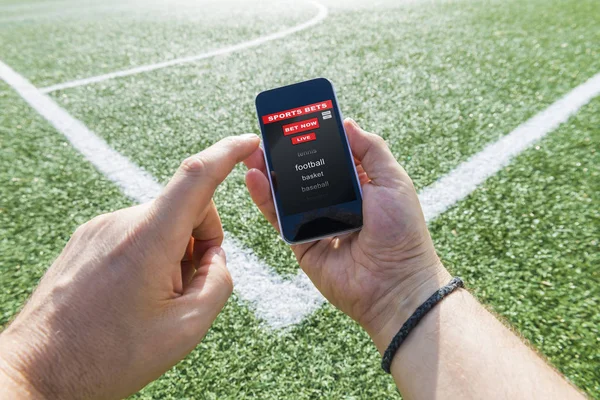 A man\'s hand holding a mobile on the green background of a socce