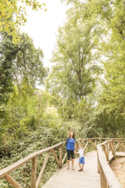Bir kadın ve bir çocuk yürüyüş yapıyor, ahşap bir yolda yürüyor..