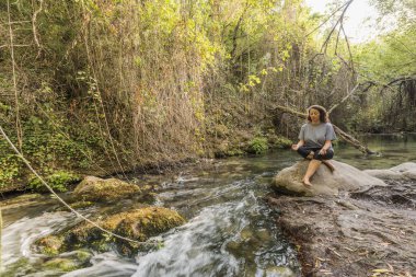 Nehrin kıyısındaki bir kayanın üzerinde meditasyon yapan kadın..