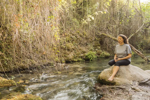 Nehrin kıyısındaki bir kayanın üzerinde meditasyon yapan kadın..
