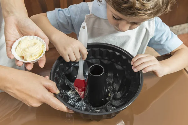 Eine Frau und ein Kind verteilen eine Kuchenform mit Butter. — Stockfoto