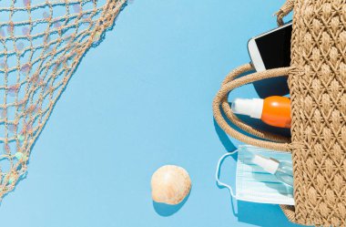 Plaj eşyalarının üst görüntüsü, yüz maskesi ve mavi arka planda hidro alkollü jel. Covid19 Coronavirus salgını sırasında yaz ve tatil konsepti.