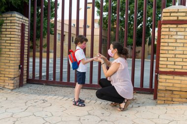 Okulun kapısındaki bir çocuğun ellerine hidro alkollü jel süren bir kadın. Covid19 salgını sırasında okuldaki yeni normalin konsepti.