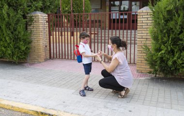 Okulun kapısındaki bir çocuğun ellerine hidro alkollü jel süren bir kadın. Covid19 salgını sırasında okuldaki yeni normalin konsepti.