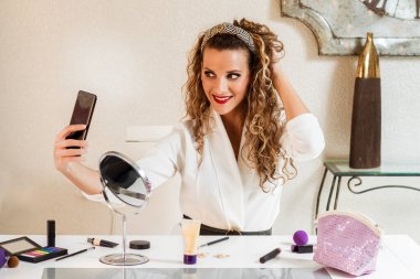 Genç sarışın beyaz kadın makyaj yaparken kendi portresini yapıyor. Sosyal medya kavramında pazarlama üzerinde etkili.