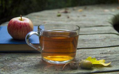 Sonbahar ahşap arka plan dinlenme fincan çay, elma ve eldiven ile okuma, parkta yürümek