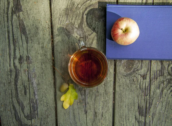 Sonbahar ahşap arka plan dinlenme fincan çay, elma ve eldiven ile okuma, parkta yürümek