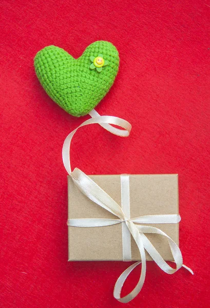 Coração de malha verde, um símbolo de amor, como um balão, com uma caixa de presente em um fundo vermelho — Fotografia de Stock