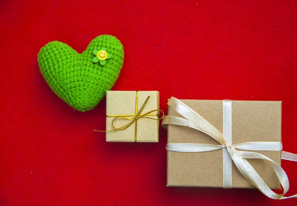 Coração de malha verde, um símbolo de amor, como um balão, com uma caixa de presente em um fundo vermelho — Fotografia de Stock