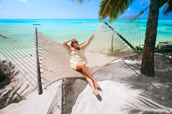 La donna si rilassa su un'amaca sulla spiaggia tra le palme vicino — Foto Stock