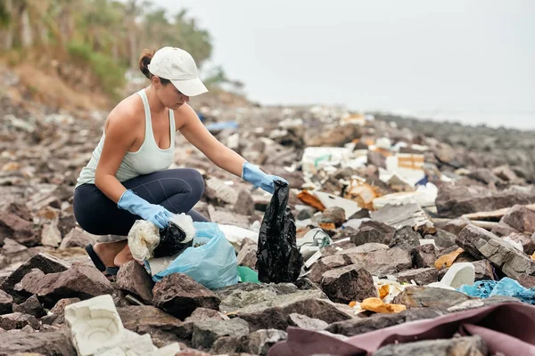 Женщина в перчатках держит пластиковый мусор на фоне морского беха — стоковое фото