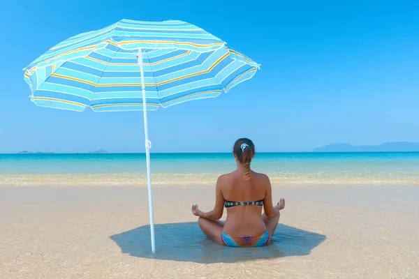 Jonge vrouw, doen yoga asana in het strand onder een paraplu. — Stockfoto