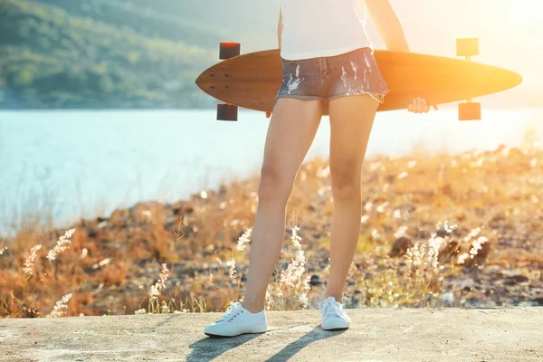 Schöne sexy junge Mädchen in kurzen Shorts steht mit Longboard bei sonnigem Wetter. — Stockfoto