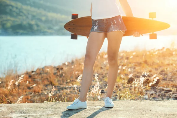 Menina sexy bonita em shorts curtos fica com longboard em tempo ensolarado . Imagem De Stock