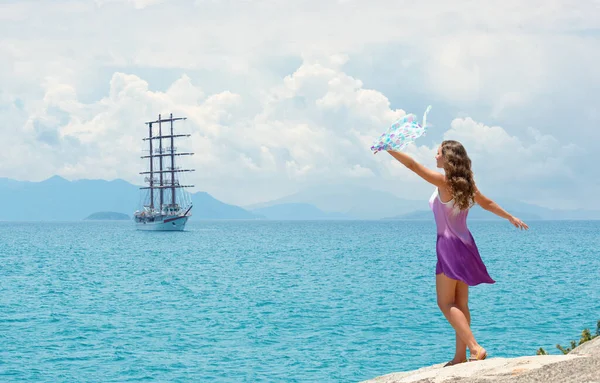 Gelukkige vrouw in jurk zwaaien zakdoek op de achtergrond van eilanden en zeilschip op zomerse zonnige dag — Stockfoto