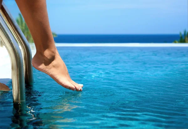 Primo piano delle gambe scalze femminili testare la temperatura della piscina in giornata di sole con sfondo sfocato. — Foto Stock