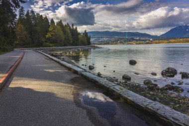 Vancouver liman ve Lions Gate Köprüsü mesafe, Stanley Park, Vancouver, British Columbia üzerinde dramatik cennet ile güneşli bir kıyı Stanley Park deniz kenarındaki sete yolu sarma