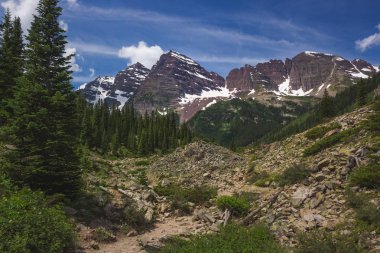 Güneşli bir günde, Colorado, Aspen yakınlarında mavi gökyüzü ile engebeli Krater Gölü patikasından görülen görkemli Maroon Bells tepeleri.