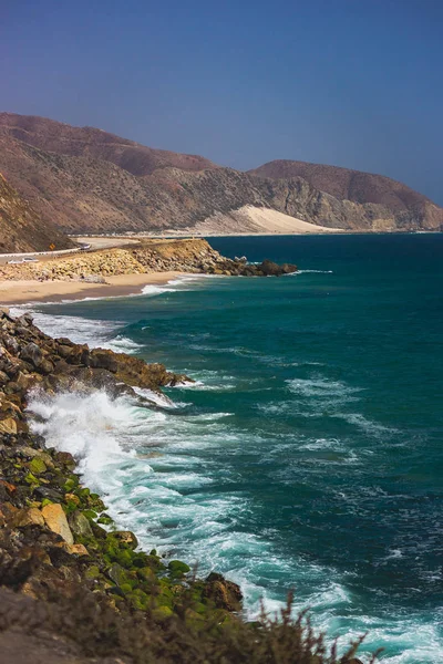 Iconic View of Pacific Coast Highway winding along the Southern California coast with the Santa Monica Mountains on one side of the road and Pacific Ocean on the other