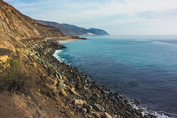 Iconic View of Pacific Coast Highway winding along the Southern California coast with the Santa Monica Mountains on one side of the road and Pacific Ocean on the other