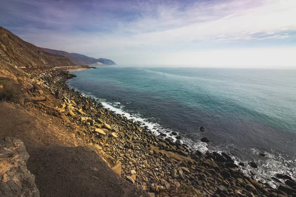 Iconic View of Pacific Coast Highway winding along the Southern California coast with the Santa Monica Mountains on one side of the road and Pacific Ocean on the other