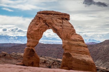 Arka planda La Sal Dağları, Moab, Utah, Arches Ulusal Parkı 'nda bulutlu bir günde ayakta duran ikonik narin kemer simgesi.
