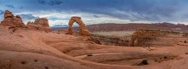 Arka planda La Sal Dağları, Moab, Utah, Arches Ulusal Parkı 'nda bulutlu bir günde ayakta duran ikonik narin kemer simgesi.