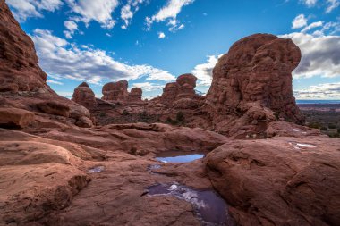 Taret kemerinin muhteşem manzarası uzun kumtaşı kuleleri ve su birikintileriyle çevrili bulutlu mavi gökyüzünü yansıtan Arches National Park, Moab, Utah