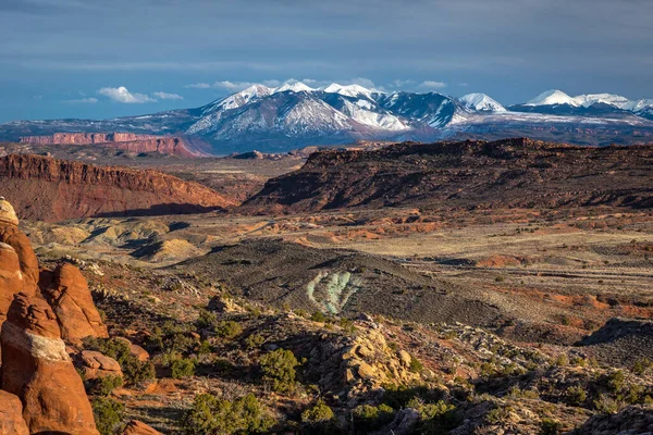 Long shadows cast across the beautiful landscape of Arches National Park at sunset with the red cliffs of Fiery Furnace in the foreground and La Sal Mountains in the distance, Moab, Utah