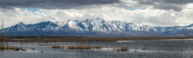 Beautiful view of snow covered Loafer Mountain with dramatic clouds in the sky, Utah Lake State Park, Provo Utah clipart