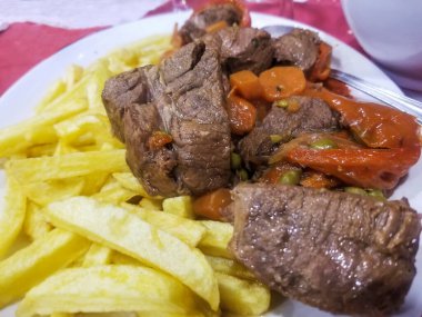 Kızarmış patates, havuç, bezelye ve dolma biberli et yahnisi servis ediliyor.