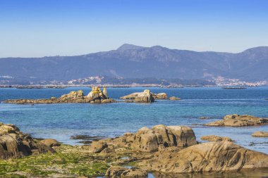 Arousa Adası 'nın kıyı şeridinde kayalıklar ve Arousa' da Curota Dağı arka planda Galiçya, İspanya