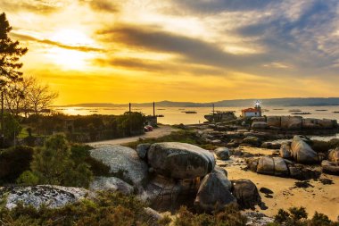 Arousa Adası 'ndaki Punta Cabalo' nun kayalık sahil şeridinde gün batımında deniz feneri.