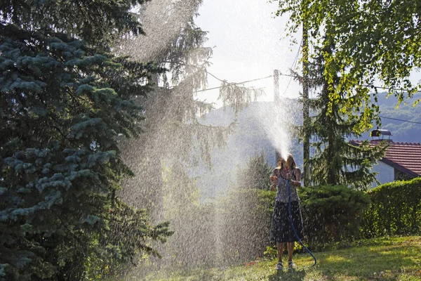 A young woman Watering a lawn in the yard of the house, a background sunlight