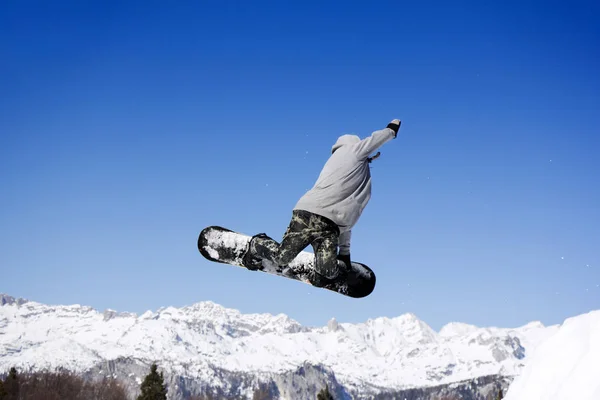 Ακραία Snowboarder άλμα στο άλμα πάνω από τα βουνά στην ηλιόλουστη μέρα — Φωτογραφία Αρχείου