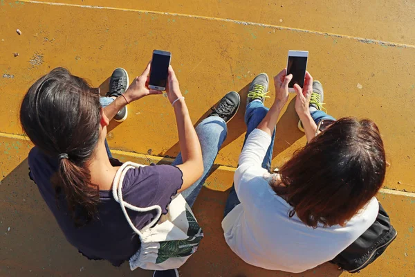 Twee jonge meisjes kijken naar slimme mobiele telefoons — Stockfoto